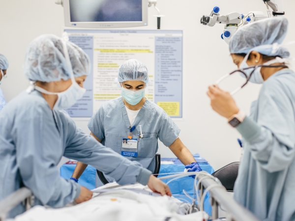 This is an image of medical personnel in scrubs standing over a bed.